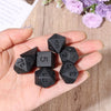 A hand holds a set of matte black polyhedral dice used for tabletop role-playing games.
