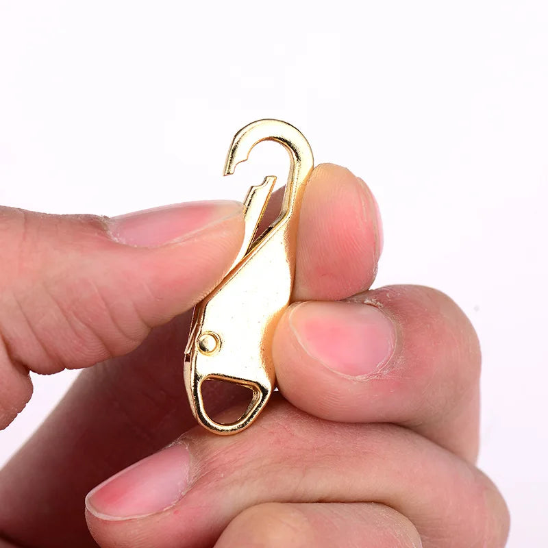 A gold-colored metal zipper slider is held between fingers against a white background.