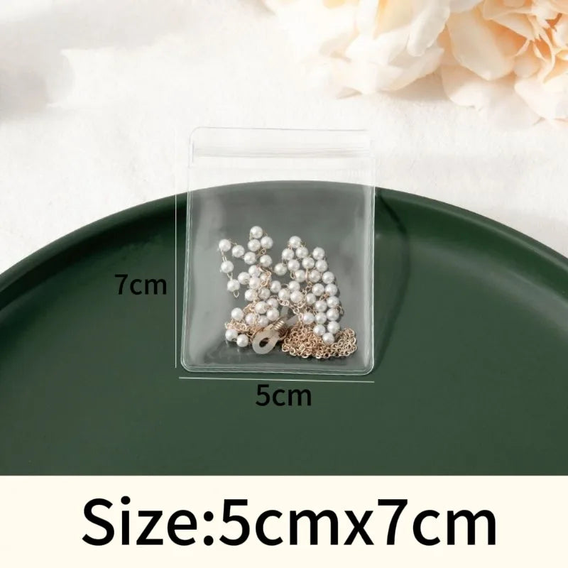A clear self-sealing jewelry storage bag containing pearl and gold-toned earrings, displayed on a dark green plate.
