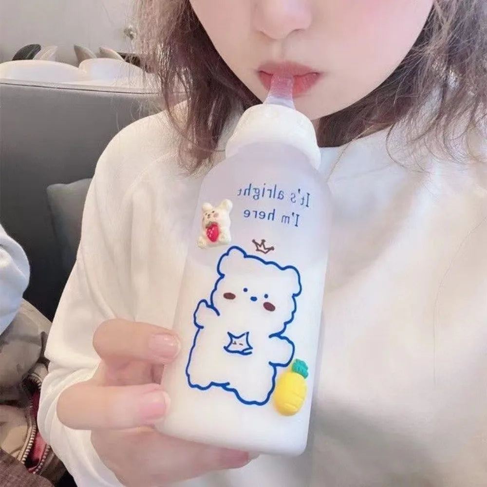 A person holds a white frosted water bottle featuring a blue outline of a bear and a strawberry, with a pink straw visible.