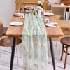 A sheer mint green tulle table runner with floral embroidery placed on a wooden dining table.