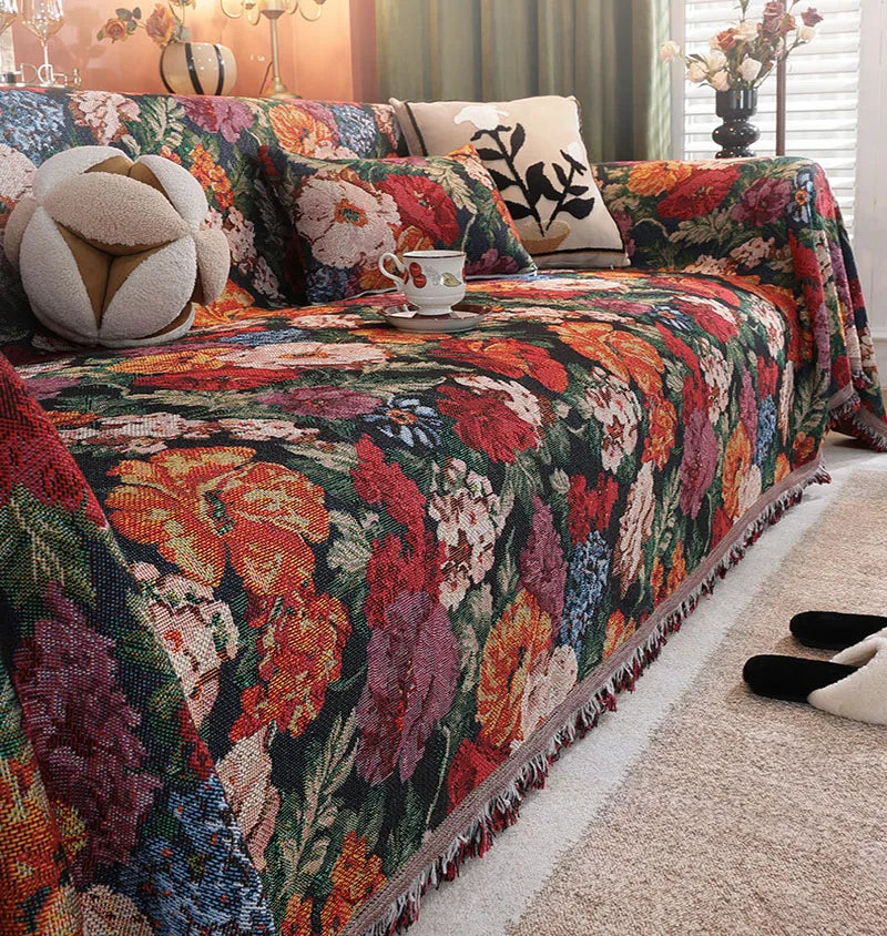 A richly colored floral jacquard sofa blanket with tassels draped over a sofa.