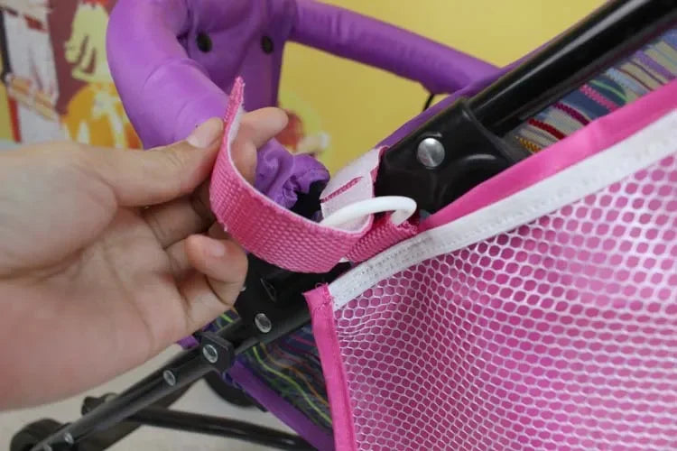 A hand is adjusting the pink mesh organizer on a purple stroller frame.