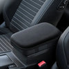A close-up view of a black car armrest cushion with a textured surface and a red button.