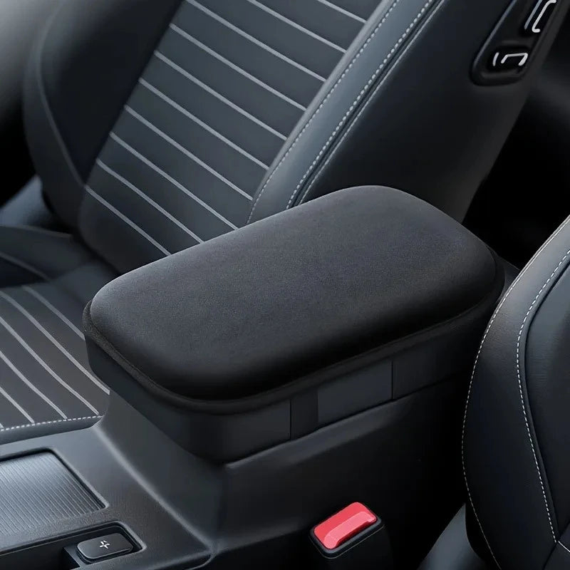A close-up view of a black car armrest cushion with a textured surface and a red button.