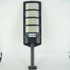 A black solar wall light fixture with multiple LED panels and a motion sensor mounted on a metal pole.