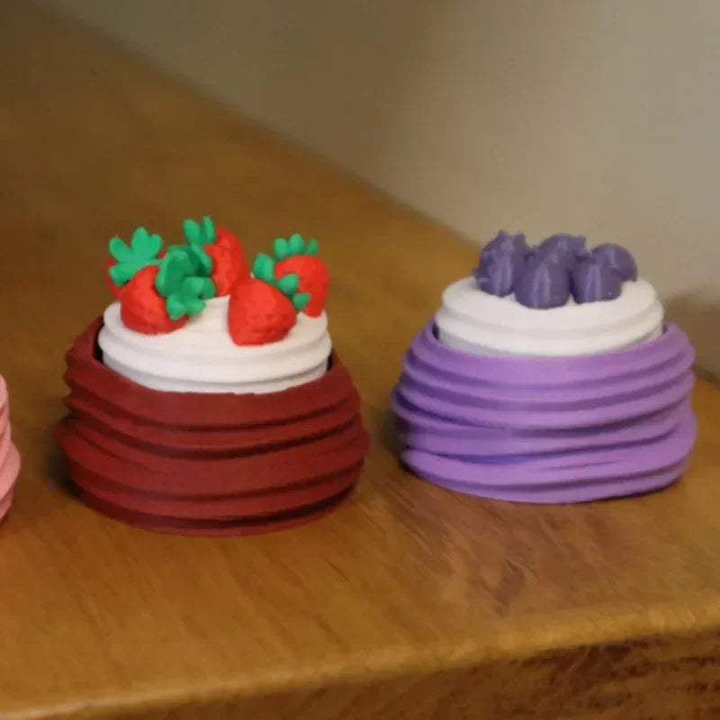 A colorful cake with strawberry and raspberry decorations is shown next to a purple cake on a wooden surface.