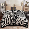 A black and white zebra print weighted plush blanket displayed on a bed with a white upholstered headboard.