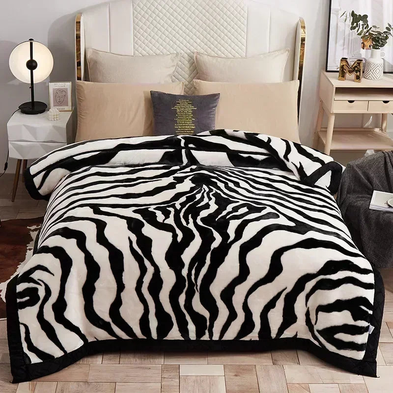 A black and white zebra print weighted plush blanket displayed on a bed with a white upholstered headboard.