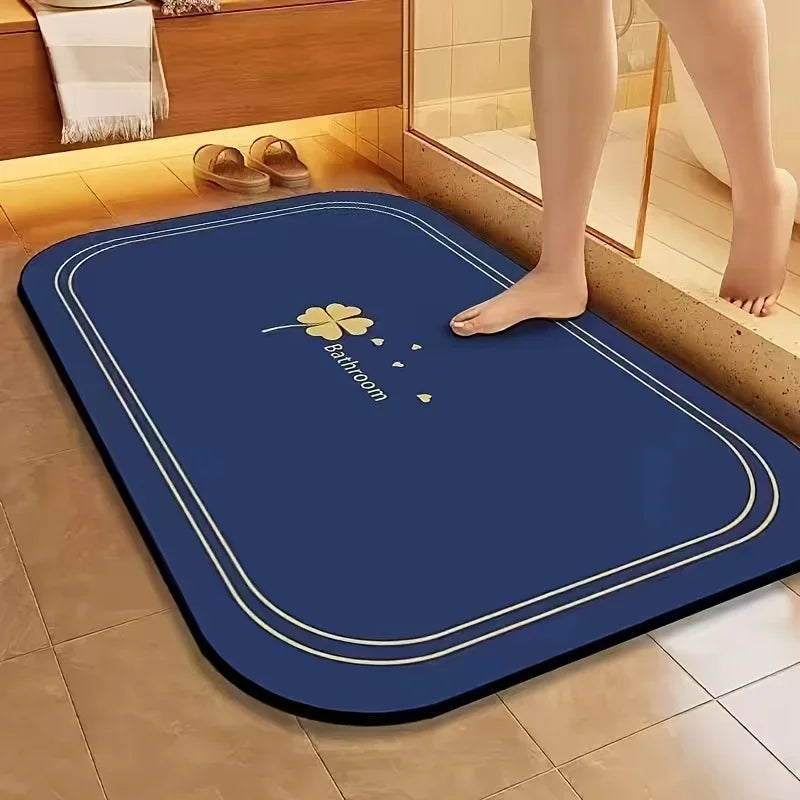 A dark blue diatomite bath mat with a gold floral design is placed on a tiled bathroom floor.