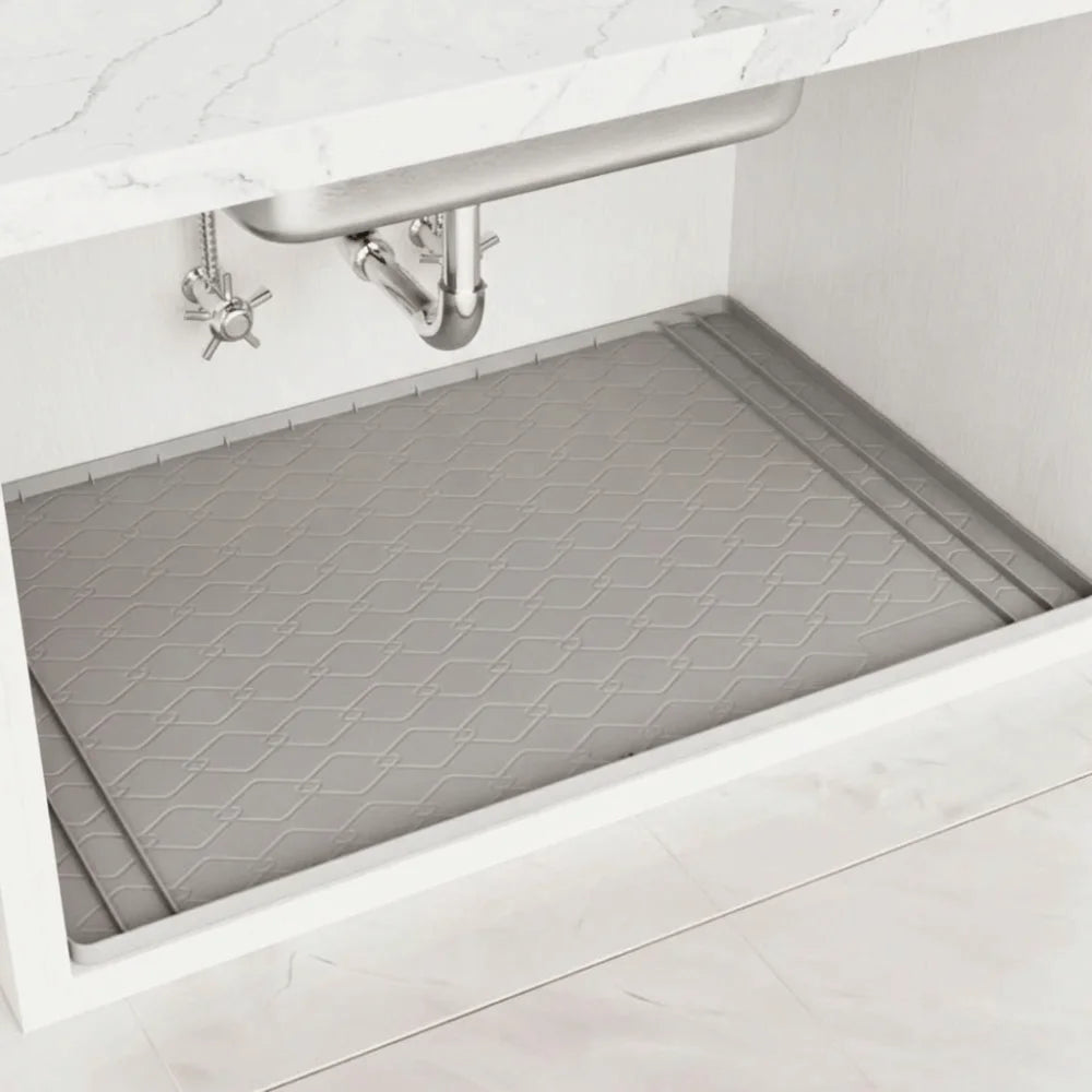 A silicone under sink cabinet protector mat is placed inside a white kitchen cabinet.