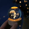 A laser engraved crystal ball night light with a silhouette of an umbrella and a figure on a wooden base.