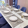A white dining table set with linen embroidered placemats, silverware, and glassware.