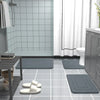 A collection of gray absorbent soft non-slip bath mats placed on a glossy tiled floor in a bathroom setting.