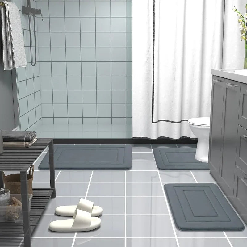 A collection of gray absorbent soft non-slip bath mats placed on a glossy tiled floor in a bathroom setting.