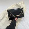 Black crocodile pattern PU envelope clutch with a gold trim and coin pocket being held against a cream jacket.
