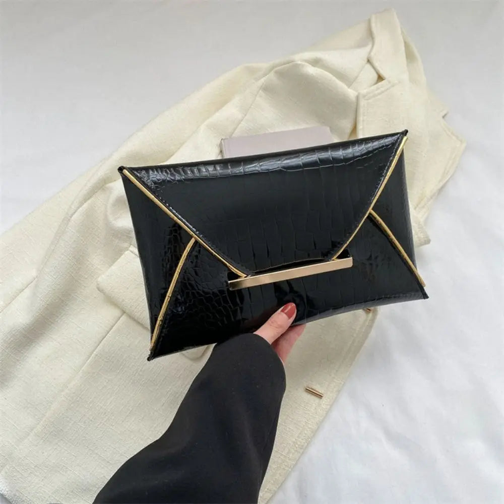 Black crocodile pattern PU envelope clutch with a gold trim and coin pocket being held against a cream jacket.
