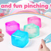 Hands are squeezing four colorful squishy stress cubes including pink, green, and blue varieties on a white surface.
