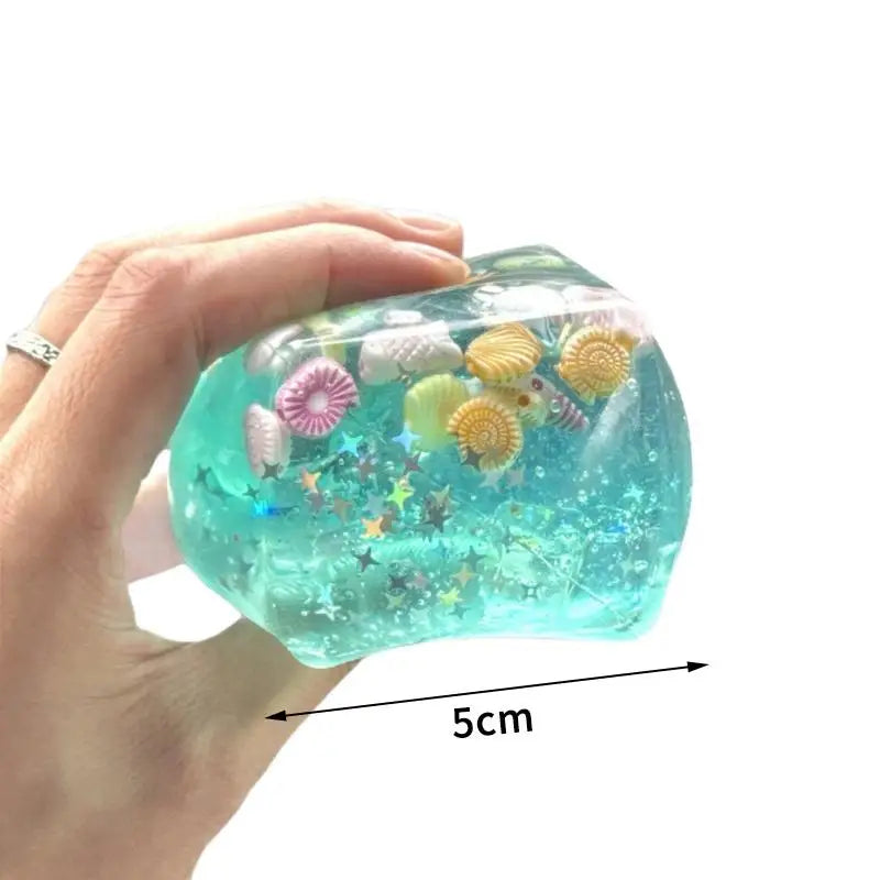 A hand holds a translucent teal glass squeeze toy filled with colorful sea creatures and glitter.
