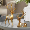 A set of two gold resin deer figurines with silver accents displayed on a gray plate.