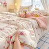 A hand is holding a pink floral quilt blanket with a soft washed finish on a bed.