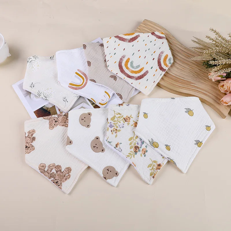 A collection of soft cotton baby bibs featuring various patterns including rainbows, leaves, and teddy bears.