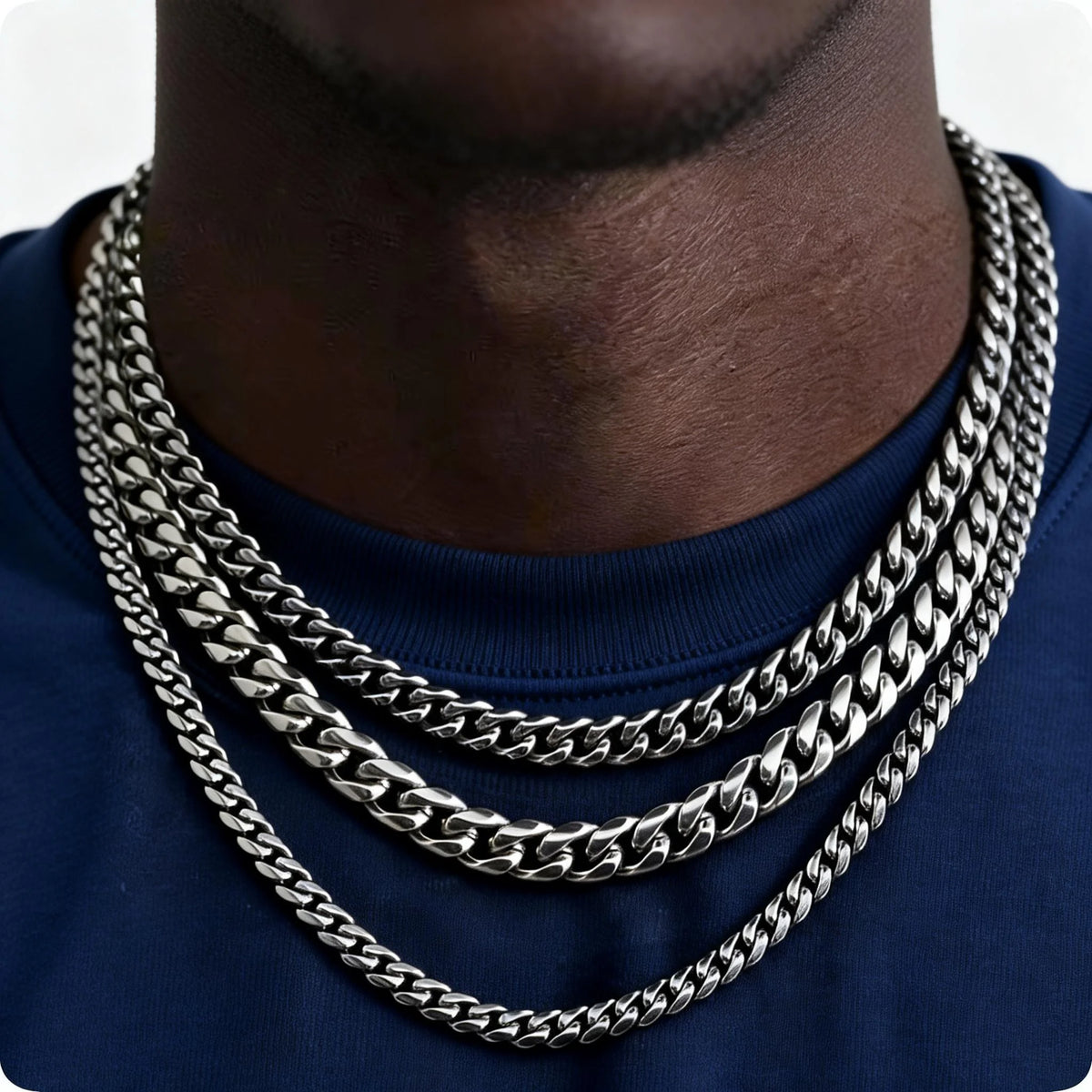 A close-up of a men's stainless steel Cuban link chain necklace worn around the neck against a dark blue shirt.