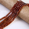 A strand of faceted amber crystal glass spacer beads is unwrapped and laid across a beige cylindrical object.