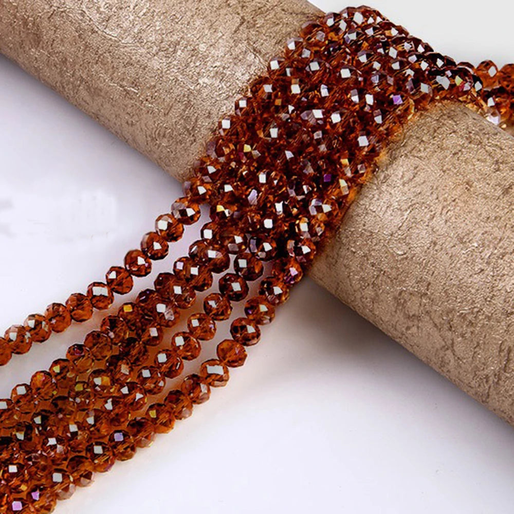 A strand of faceted amber crystal glass spacer beads is unwrapped and laid across a beige cylindrical object.