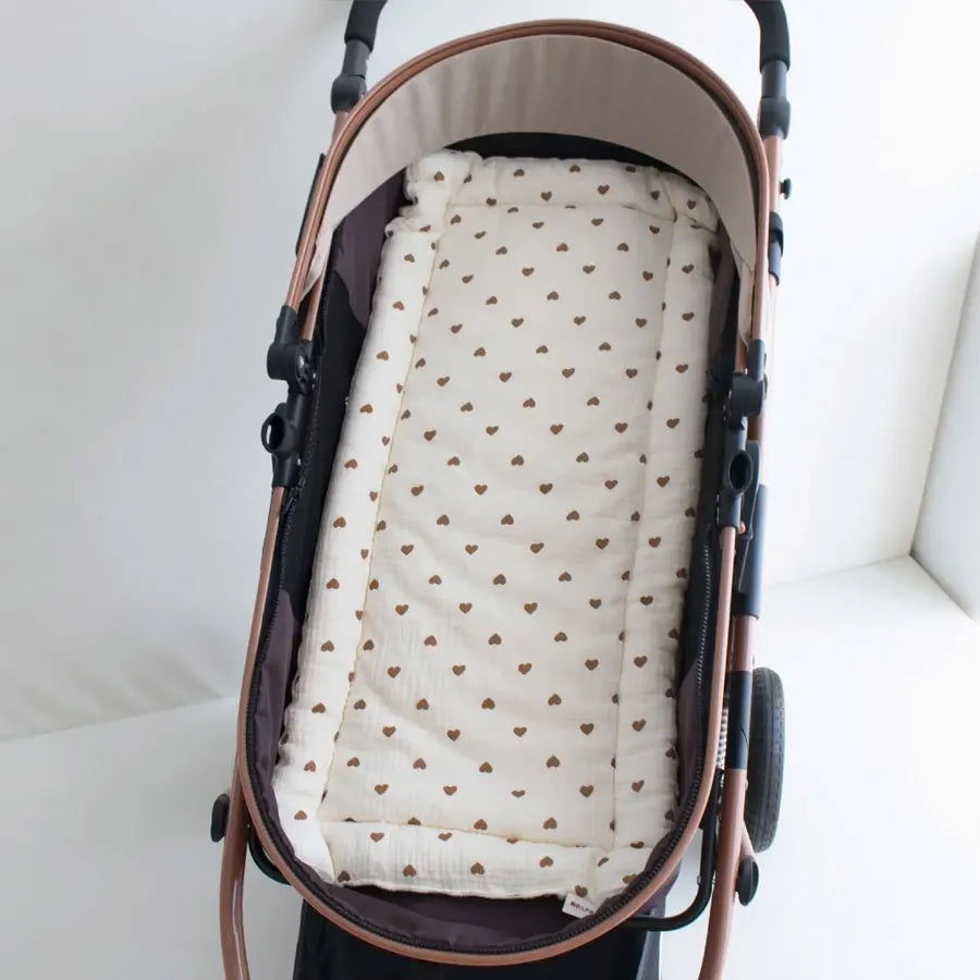 A beige and brown stroller cushion with a pattern of small brown bear hearts.