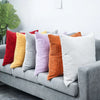 A set of nine striped velvet corduroy cushion covers in various shades of red, yellow, purple, and orange arranged on a gray 