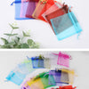 A collection of colorful organza drawstring jewelry gift bags in various shades of pink, red, blue, and green.