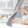 A hand is holding a flexible silicone sink splash guard with a suction cup on a white countertop.