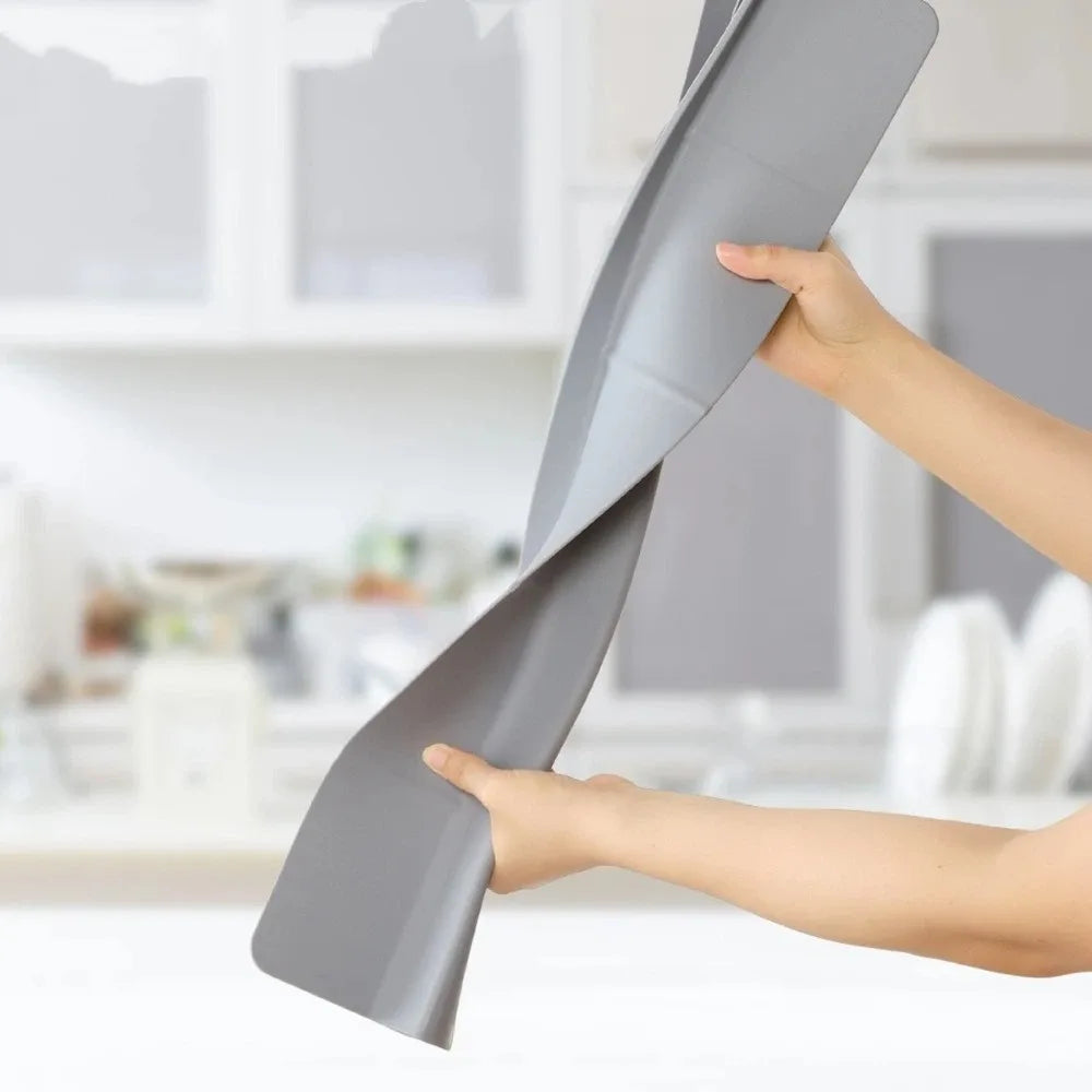 A hand is holding a flexible silicone sink splash guard with a suction cup on a white countertop.