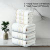 A stack of three white hand towels and three bath towels with gold accents displayed on a marble surface.