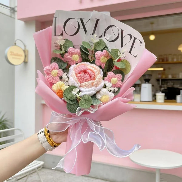 A bouquet of pink and white crochet artificial flowers wrapped in pink paper and tied with a sheer ribbon.