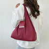 A person is holding a maroon retractable keychain tote bag with a silver rectangular pouch attached to the front.