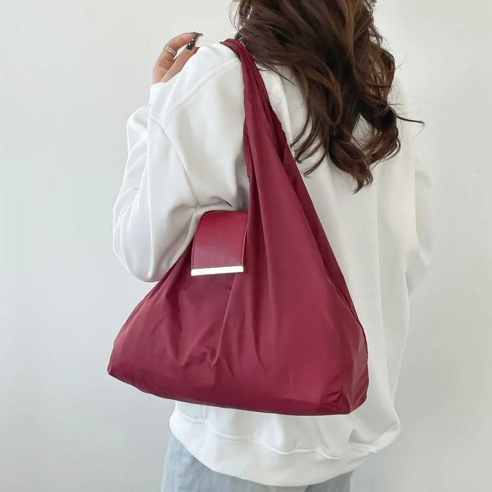 A person is holding a maroon retractable keychain tote bag with a silver rectangular pouch attached to the front.