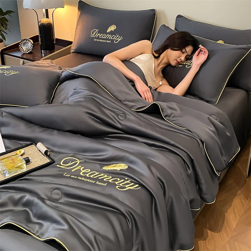 A woman rests on a gray comforter featuring the Dreamcity embroidery, with a lamp and decorative items nearby.