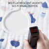 A hand holds a black electronic device against a white cotton muslin bib, with text stating no fluorescent agents or formalde