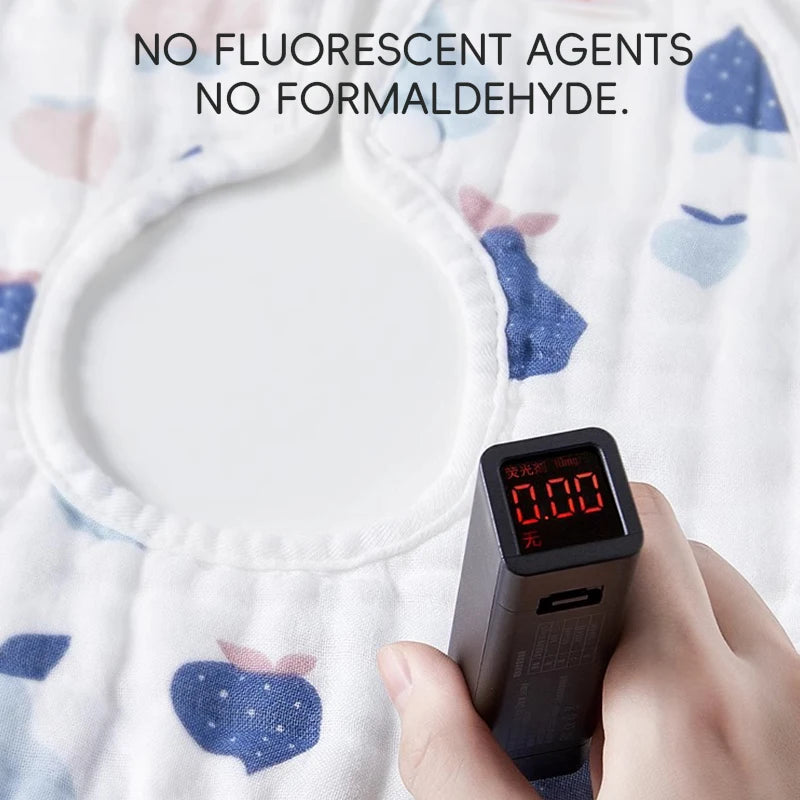 A hand holds a black electronic device against a white cotton muslin bib, with text stating no fluorescent agents or formalde