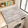 A close-up view of a wood grain waterproof washer and dryer mat placed inside a white washing machine.