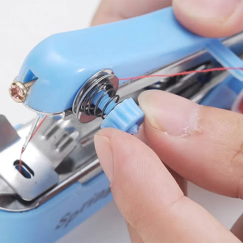A hand is using a portable blue handheld sewing machine to thread a needle with red thread.