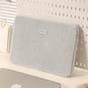 Una funda protectora gris claro para portátil, apoyada sobre una superficie blanca.