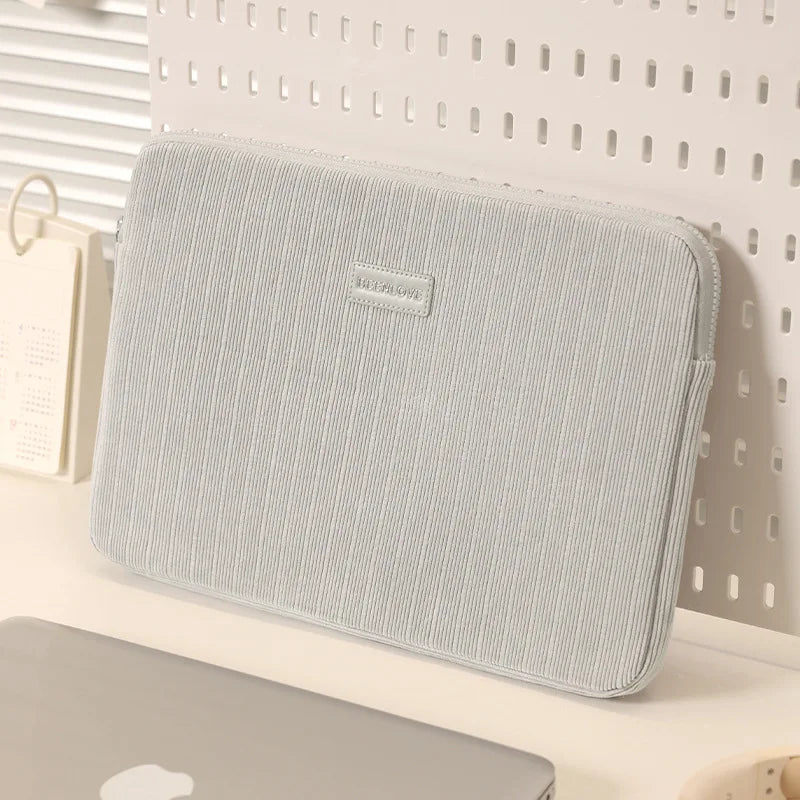 Una funda protectora gris claro para portátil, apoyada sobre una superficie blanca.