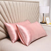 Una funda de almohada de satén de seda rosa se muestra en una cama con cabecero acolchado y una lámpara de noche.