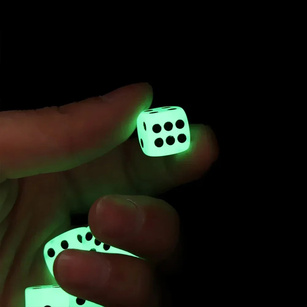 A hand holds a glow-in-the-dark acrylic dice set, with some dice illuminated and others dark against a black background.