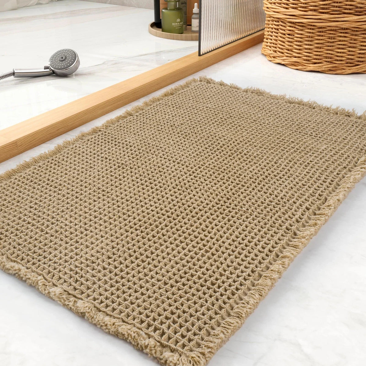 A beige waffle texture bath mat is displayed on a white marble surface next to wooden slats and a wicker basket.