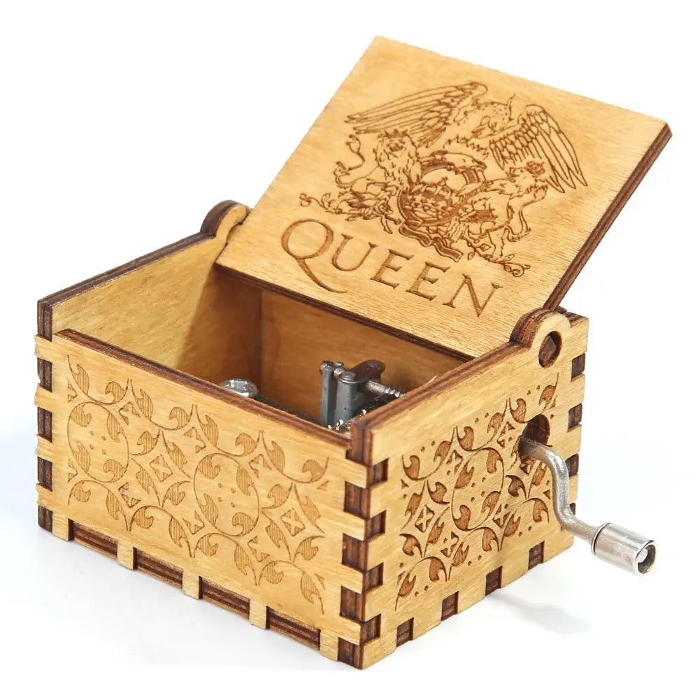 A light brown wooden music box with an ornate lid featuring a winged figure and the word QUEEN
