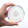 A hand holds a circular arrangement of colorful round pearl straight pins for sewing and crafts.